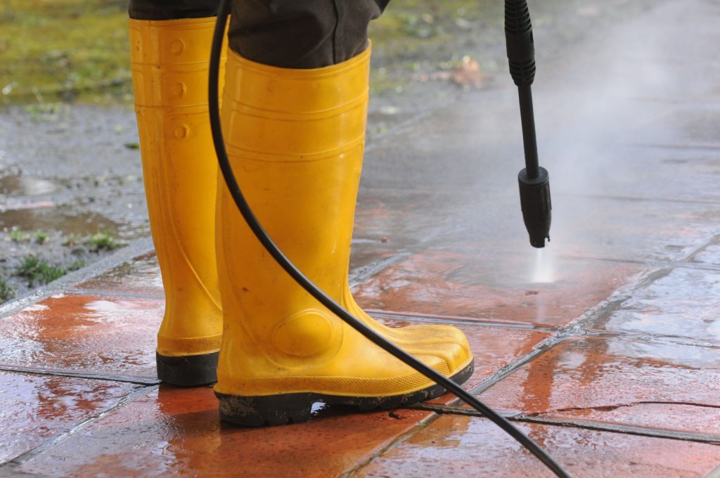 person-wearing-yellow-rubber-boots-with-high-pressure-water-nozzle-cleaning-dirt-tiles